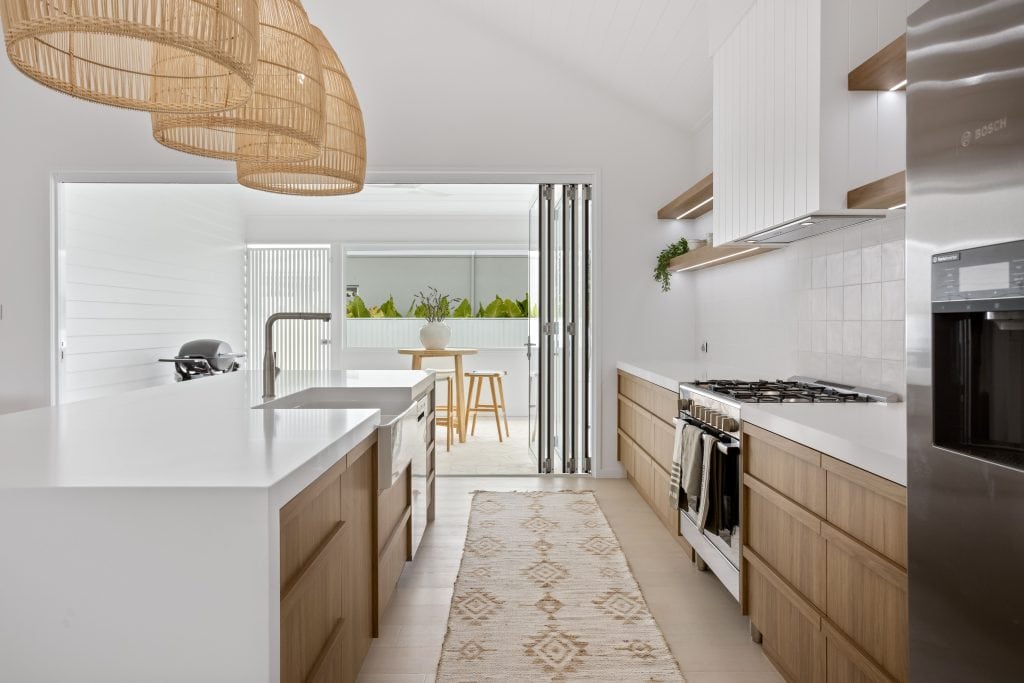 Inviting kitchen view featuring a white quartz island, light wood cabinetry, and oversized bamboo pendant lights, with a bi-fold window opening to an outdoor bar area.