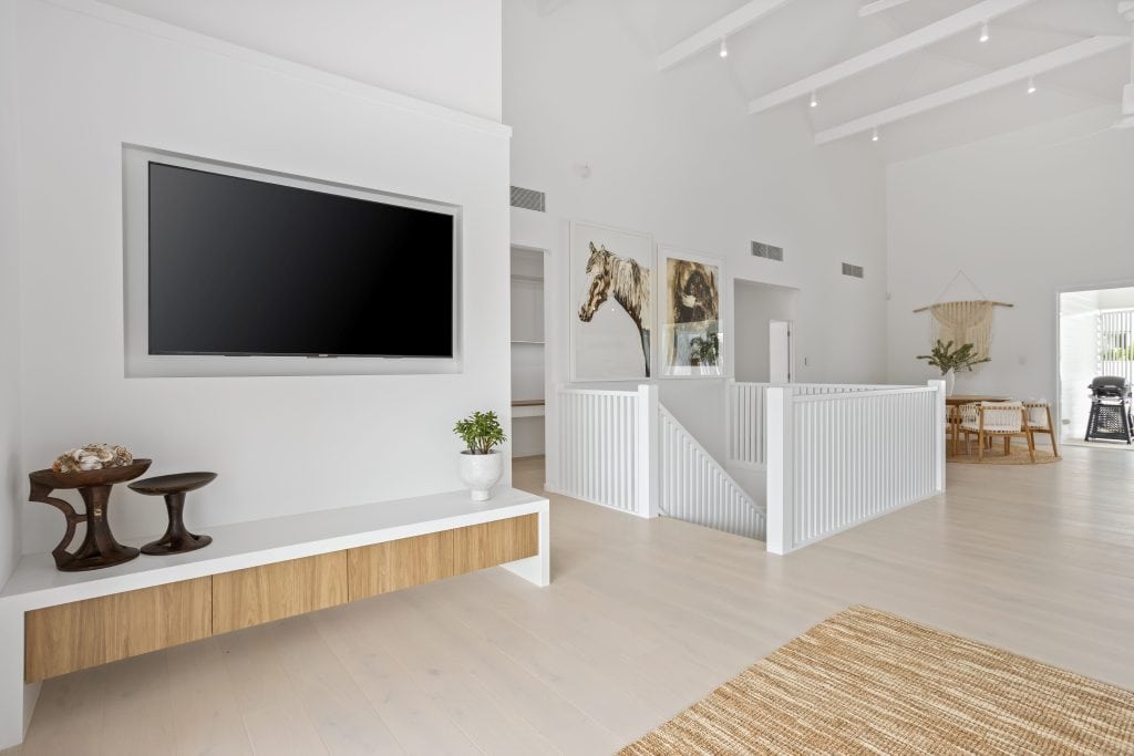 Spacious living room with high ceilings featuring a wall-mounted TV, minimalist furniture, and elegant art pieces, with abundant natural light flowing through white sheer curtains.