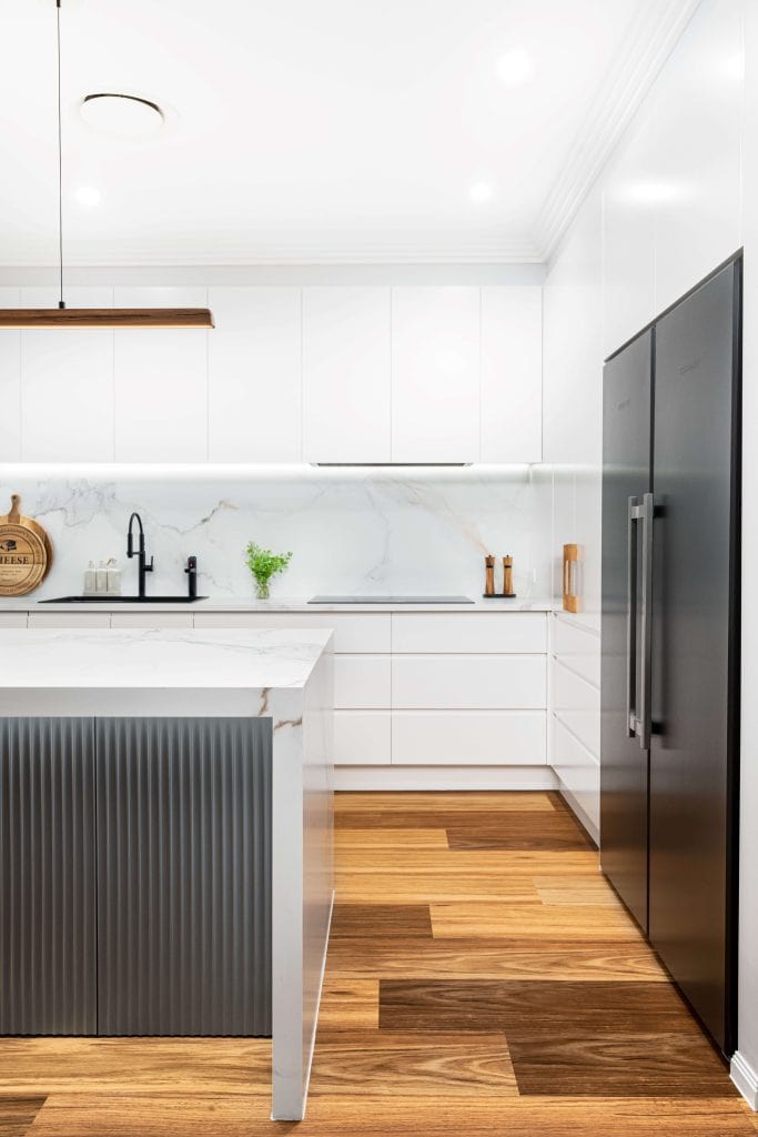 Sleek and modern white kitchen in Brisbane featuring a marble countertop island with ribbed detailing, matte black appliances, and wooden flooring. The design includes white cabinetry, a black matte faucet, and integrated appliances, creating a clean and minimalist aesthetic with subtle wood accents.