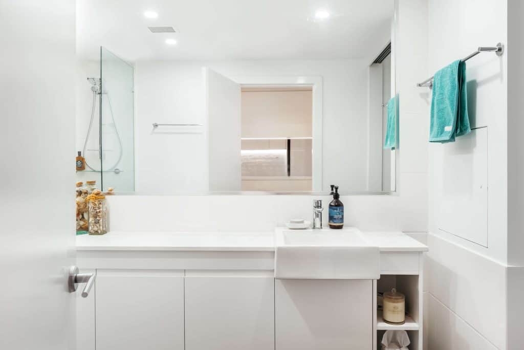 A tranquil bathroom setting in New Farm, Brisbane, with a white vanity, marble countertop, and a walk-in shower visible through a clear glass partition, complemented by soft aqua towels and natural decor accents.