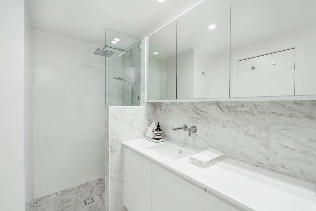 A pristine bathroom in New Farm, Brisbane, featuring floor-to-ceiling marble tiles, a wall-mounted vanity with ample storage, and a spacious glass-encased shower area, reflecting a modern, luxurious design.