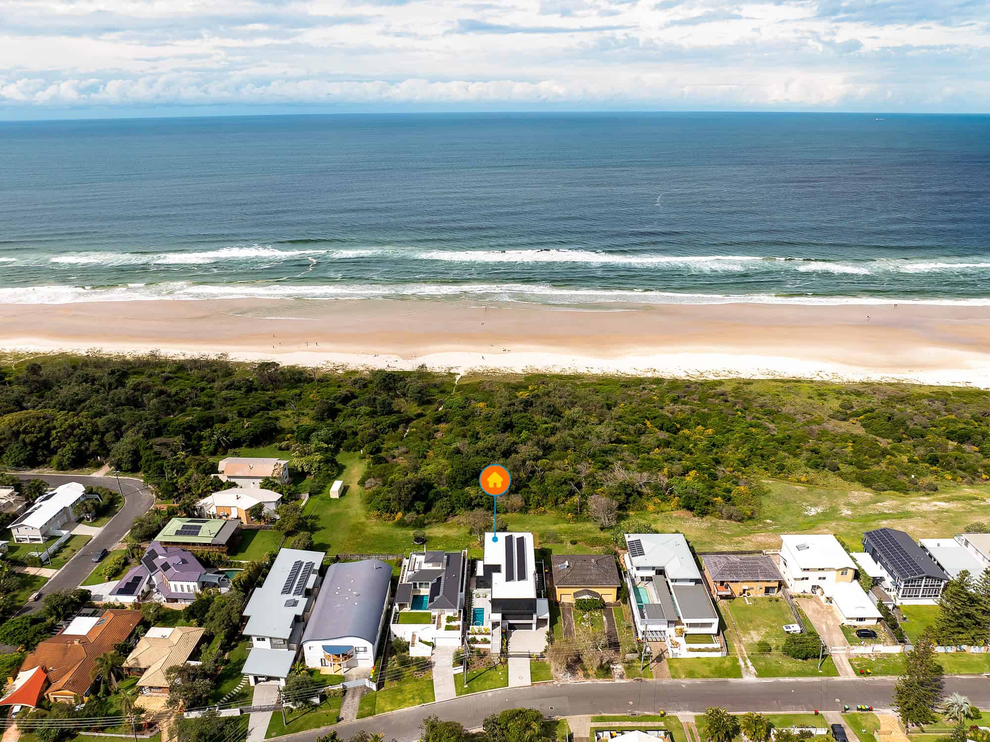 An aerial view of Pottsville, showcasing modern homes along the coastline with the vast ocean and sandy beach stretching into the distance. The lush greenery of the coastal vegetation contrasts with the blue waters and white sands, highlighting the serene beauty of this coastal town.