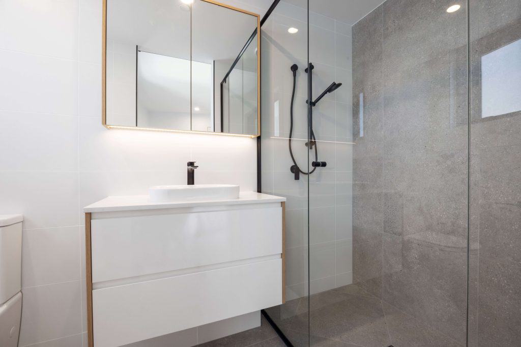 Modern bathroom with a frameless glass shower, matte black fixtures, and a sleek vanity with a vessel sink under an illuminated mirror.