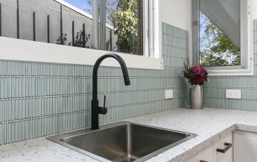 Stainless sink with black tap and blue wall tiles in a modern kitchen renovation after photo