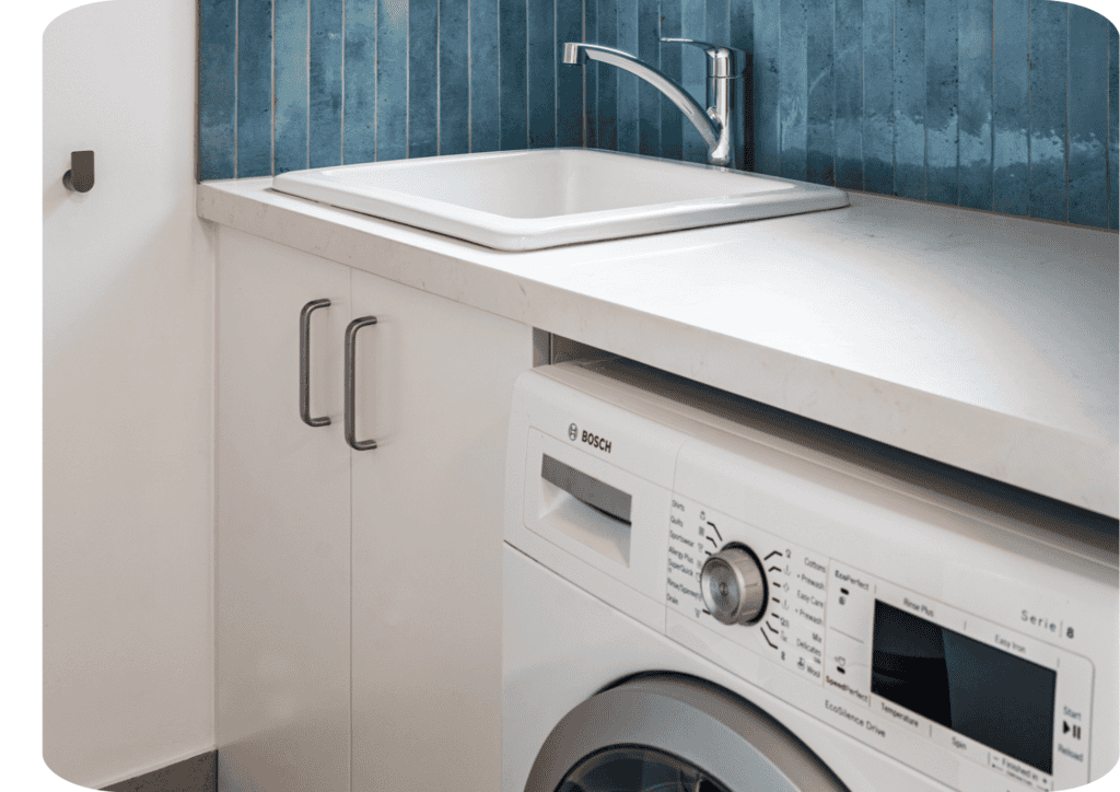 Compact modern laundry with a Bosch front-loading washing machine, white cabinetry, marble-look benchtop, and a deep utility sink against a vertical blue tile splashback.